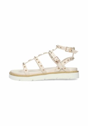 Sandalo flat beige con cinturini, borchie dorate, doppia fibbia alla caviglia e a metà piede, suola bianca spessa con dettagli di borchie dorate.