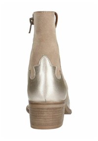 Stivaletto in suede beige con accenti dorati metallici e design a ondine sui lati. Dotato di un tacco corto e chiusura con cerniera.