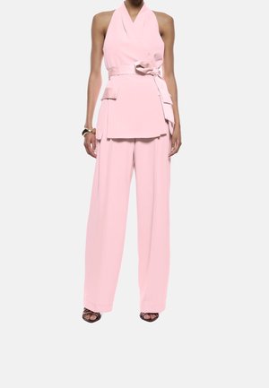 Lichtroze tweedelig outfit met een haltertop met strikdetail, wijd uitlopende broek en instapschoenen met hak. Gladde stof.