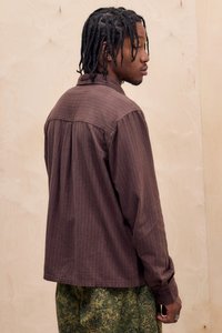 Camicia marrone a righe con un fit rilassato, dotata di colletto con bottoni e maniche lunghe, abbinata a pantaloni con motivo mimetico.