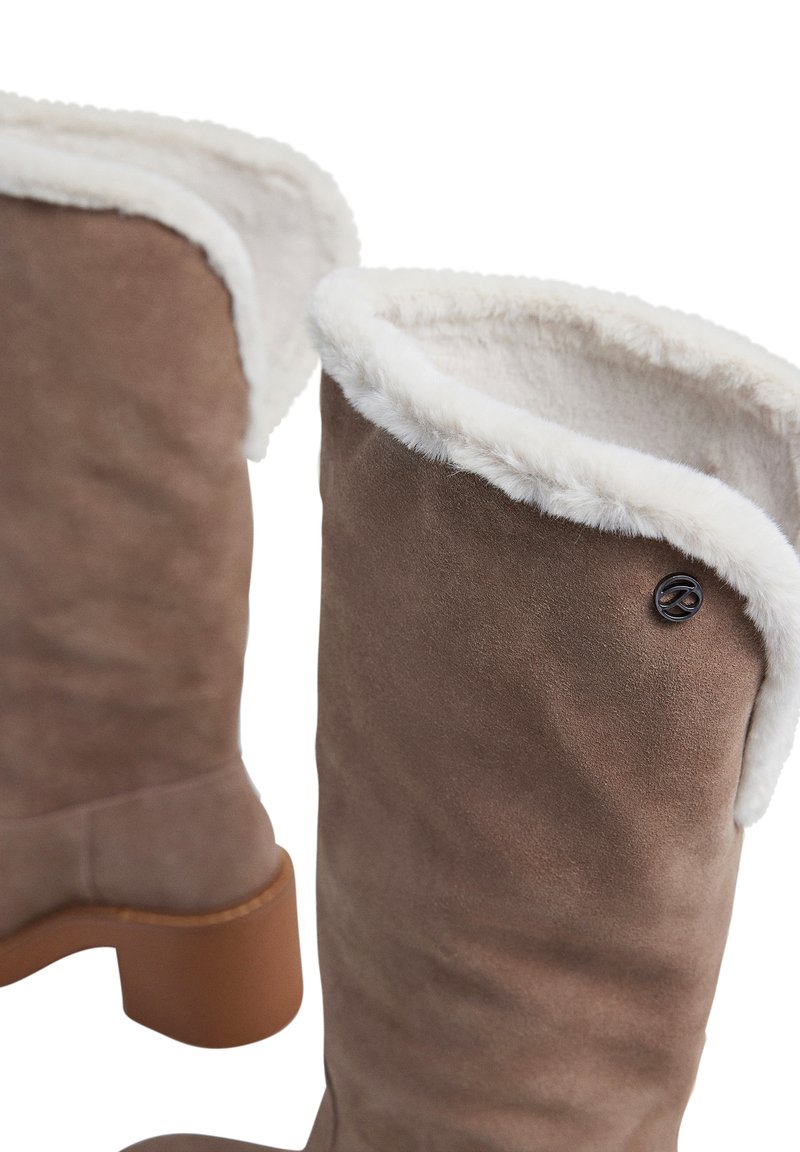 Braune Wildlederstiefel mit weißem Kunstfellfutter, klobigem, beigen Absatz und einem schwarzen Logostreifen an der Seite. Sie haben eine glatte Textur.