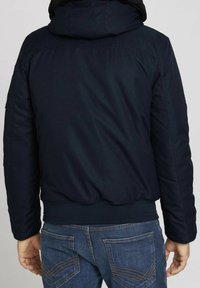 Giubbotto imbottito blu navy con cappuccio, tessuto testurizzato, orlo e polsini a coste. Presenta una finitura liscia e offre uno stile casual.