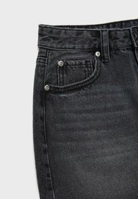 Nærbillede af sorte denimjeans, der viser forlomme, lille møntlomme, bæltestrop og metalnitter på tekstureret stof.