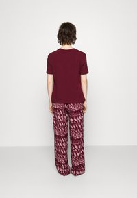 Bordo majica kratkih rukava u kombinaciji s širokim hlačama s uzorkom u nijansama tamnocrvene i ružičaste boje u tie-dye dizajnu.