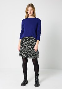 Blå sweater, sort og grå zebra-Mønsteret nederdel med flæser. Modellen har kombineret med sorte ankelstøvler og sorte strømpebukser.