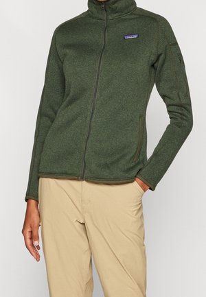 Donkergroene fleecjacket met een hoge kraag, een ritssluiting aan de voorkant en twee zijzakken. Voorzien van een logopatch op de linkerkant van de borst en geribde manchetten.