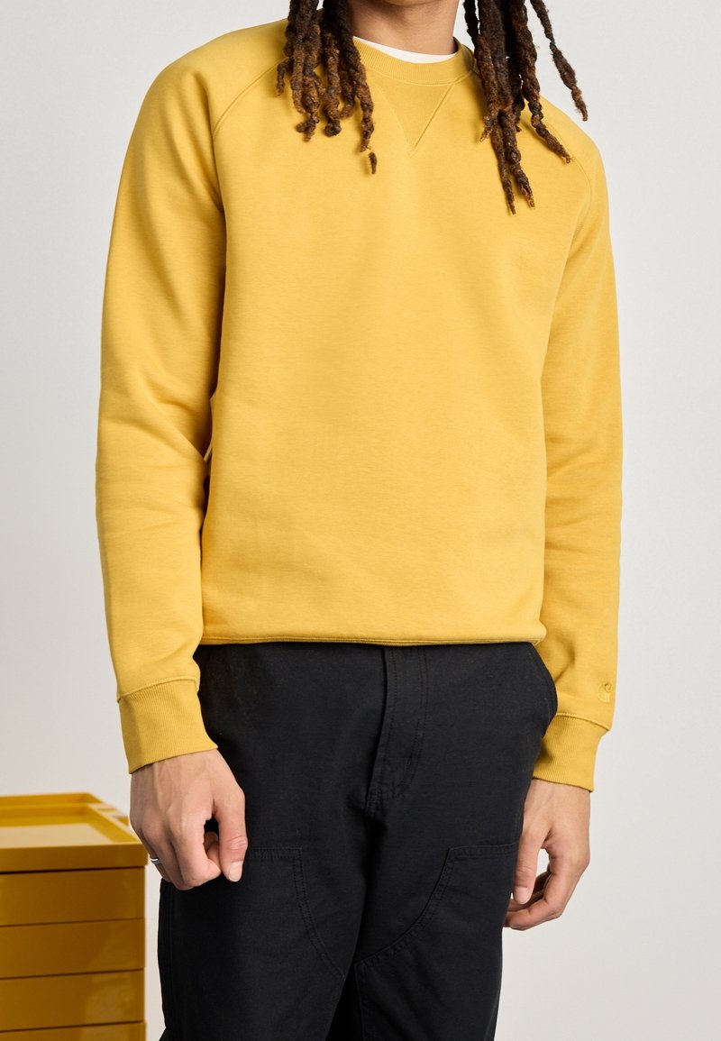 Felpa gialla con scollatura a girocollo e polsini a coste, abbinata a pantaloni neri. Texture liscia con vestibilità comoda.