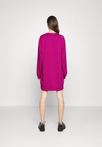 Oversized sweter w intensywnym magencie z długimi rękawami, ribbowymi mankietami i okrągłym dołem. Posiada detal szycia na ramieniu.