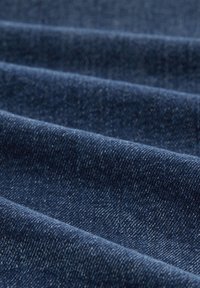 Tessuto denim di colore blu scuro con una superficie strutturata, caratterizzato da schemi di tessitura visibili e sottili variazioni di tonalità. Piegato in più onde.