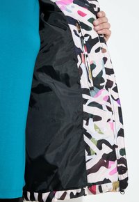 Veste camouflage multicolore avec un extérieur lisse et léger et des motifs vibrants. Dispose d'une poche zippée à l'intérieur gauche.