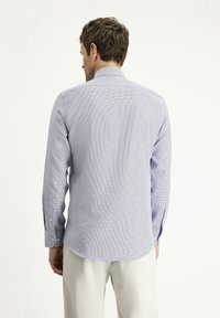 Camicia azzurra chiara con un pattern testurizzato, maniche lunghe e orlo curvo. Presenta polsini con bottoni classici e colletto aperto.