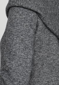 Harmaa neulottu kangas, jossa on teksturoidun näköinen pinta, huppu ja pehmeä viimeistely. Materiaali on kevyt ja sopii rentoon käyttöön.