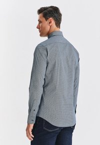 Niebieska koszula z długim rękawem w wzory, z kołnierzykiem rozłożonym, zaszewką z tyłu i detalami mankietów, wykonana z lekkiego materiału.