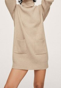 Dress in maglia a coste beige con colletto alto, due tasche frontali e vestibilità rilassata, con orlo che si ferma sopra le cosce.