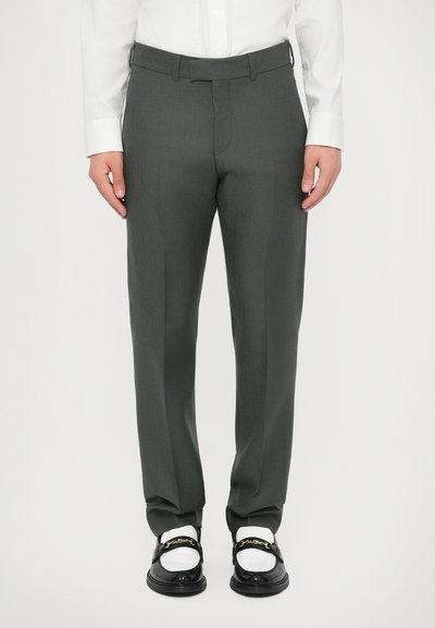 Pantaloni su misura di un verde scuro, con una texture liscia, vestibilità dritta e passanti per cintura, abbinati a mocassini neri e calzini bianchi.