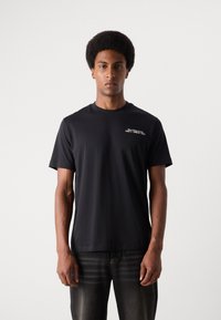 Schwarzes T-Shirt aus weichem Stoff, mit kurzen Ärmeln und Rundhalsausschnitt. Text "CAN'T TOUCH THIS" in Weiß auf der linken Brustseite aufgedruckt.
