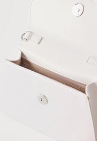 Λευκή δερμάτινη τσάντα με ανοιχτό καπάκι που αποκαλύπτει μπεζ εσωτερικό, ασημένιο μαγνητικό κούμπωμα και ραφές διακόσμησης.