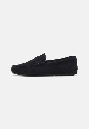 Mocassin en daim noir à bout arrondi, détails cousus, talon bas et logo discret « BOSS » sur la bride latérale, vue de côté sur fond blanc.