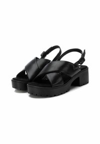 Sandalias negras de cuero con diseño entrecruzado, suela de plataforma gruesa y correa ajustable. Suela texturizada para mayor agarre.