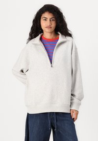 Gray zip-up sweatshirt with a relaxed fit, featuring a high collar and ribbed cuffs, layered over a red and blue striped shirt.