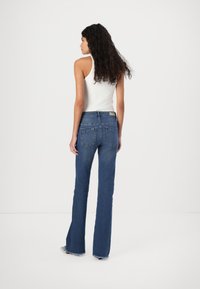 Jeans azuis com corte flare e cintura média, apresentando um design clássico de cinco bolsos e bainha desfiada. O tecido tem uma textura suave.