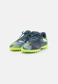 Scarpe sportive blu e verdi con superficie texturizzata, pattern dinamici e tacchetti in gomma per la trazione. Presentano lacci e un logo di marca.