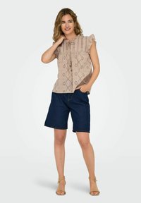 Helles beiges Rüschenshirt mit Lochmuster, kombiniert mit dunkelblauen Jeansshorts. Das Outfit hat einen lässigen Schnitt und ein schlichtes Design.
