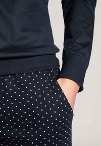 Navy sweatshirt with ribbed cuffs paired with black pants featuring a polka dot pattern in white and light pink. Smooth fabric texture.