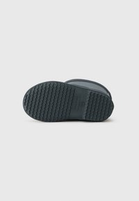Semelle de botte en caoutchouc bleue avec un motif de crampons en zigzag, dotée d'un label de marque et d'un talon lisse et arrondi.