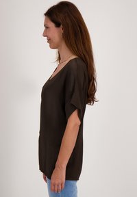 Bruine V-hals top met korte mouwen, relaxte pasvorm, soepele textuur en een subtiele glans, gecombineerd met lichtblauwe jeans.