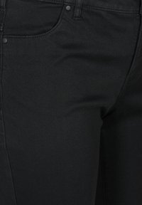 Jeans de mezclilla negra con una textura suave, corte ajustado, diseño tradicional de cinco bolsillos y costuras contrastantes a lo largo de las costuras.