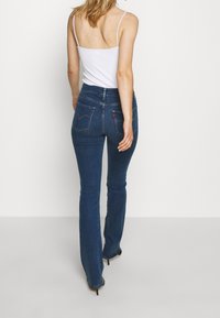 Tmavě modré džínové zvonové kalhoty s vysokým pasem, obsahující dvě zadní kapsy, značkovou etiketu a slim fit střih přes stehna.