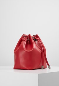 Rød læder spandtaske med en glat tekstur, snøret lukning og sølvhardware. Har en afrundet bund og justerbare stropper.