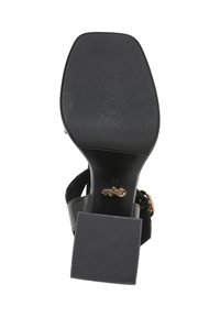 Sandale noire pour femme avec un talon carré et une semelle texturée, vue par le dessous, montrant un logo de marque doré et une boucle sur la bride.