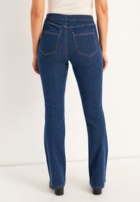 Siniset farkut joustavalla vyötäröllä, kahdella takataskulla ja suoranlahkeisella leikkauksella. Saumojen yksityiskohtia näkyy taskuissa ja helmoissa.