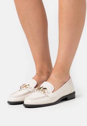 Mocassins en cuir blanc avec une boucle dorée, dotés d’un bout arrondi et d’un petit talon noir. Texture lisse et design minimaliste.