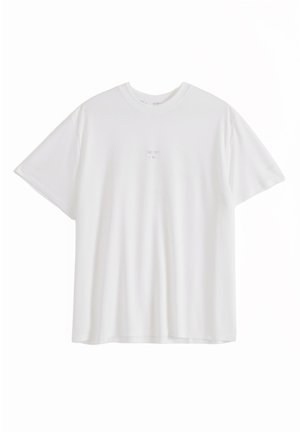 Camiseta blanca de manga corta con cuello redondo, con un pequeño y sutil logo o texto en el centro del pecho, lisa y holgada.