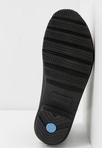 Semelle de chaussure en caoutchouc noir présentant un motif de semelle texturé, des accents moulés et un détail de logo bleu avec le nom de la marque "HUNTER."
