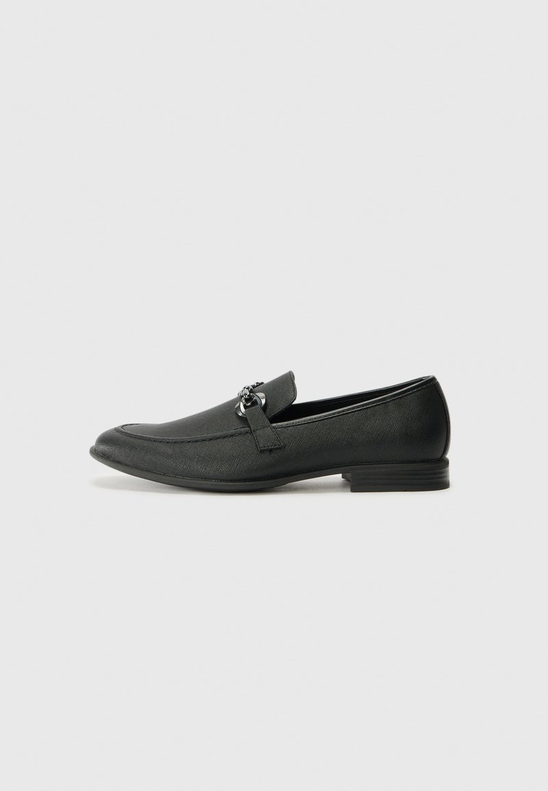 Mocasines de cuero negro con punta redondeada, superficie texturizada, banda decorativa y acentos sutiles. Tacón bajo apilado.