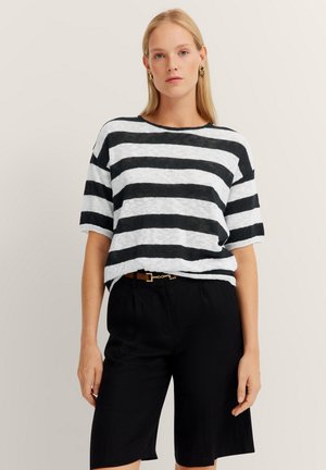 Black and white striped short-sleeve top, lightweight fabric, relaxed fit, round neckline. Paired with black shorts and a belt.