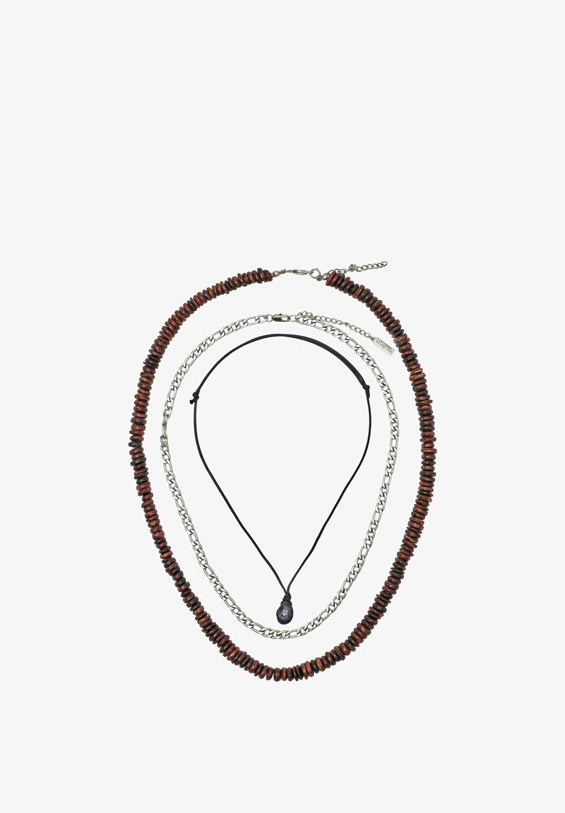 Trois colliers superposés : extérieur avec des perles en bois brun foncé, milieu avec des maillons de chaîne en argent, intérieur avec un cordon noir et un pendentif en pierre noire.