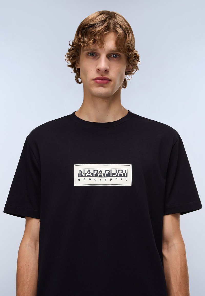 Schwarzes Baumwoll-T-Shirt mit einem rechteckigen weißen Logo, das den Text "NAPAPURI" und "geographic" zeigt, kurzen Ärmeln und einem Rundhalsausschnitt.
