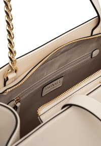 Borsa beige con tracolla a catena dorata, scomparti con zip e rifiniture nere. L'interno presenta un tessuto liscio e un'etichetta contrassegnata "TWINGSET."