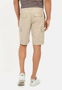 Beige cargoshorts met meerdere zakken, een relaxte pasvorm en een knielange snit, gedragen met witte sneakers. Achteraanzicht weergegeven.