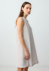 Lichtgrijze mouwloze jurk met een A-lijn model, gemaakt van zachte stof, met een ronde halslijn en een zoom die boven de knie valt.
