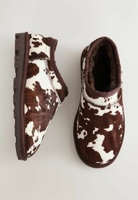 Stivali slip-on con stampa di mucca marrone e bianca, con fodera interna in pelliccia morbida, suola in gomma e dettagli di cucitura in contrasto lungo le cuciture.