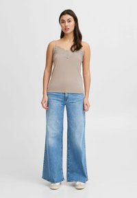 Camiseta sin mangas beige con encaje, combinada con jeans de pierna ancha azul claro. La camiseta tiene tirantes finos y una textura suave.