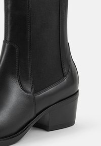 Bottines noires en cuir avec une finition lisse, des panneaux latéraux élastiques, un bout arrondi et un talon bas.