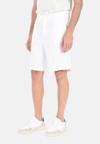 Shorts bianchi in lino con vita elastica e cordino, caratterizzati da una vestibilità comoda. In abbinamento, sneakers bianche con dettagli blu.