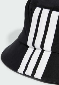 Zwarte bucket hat met drie verticale witte strepen. Gemaakt van katoen met een gladde textuur en een brede, schuin lopende rand.